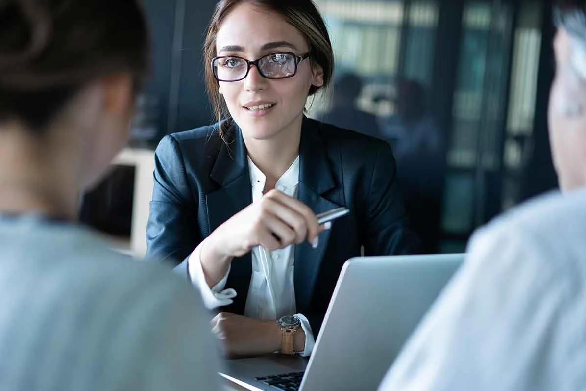 Eine Zahnärztin und ihr Niederlassungsberater sitzen beim Bankgespräch zur Finanzierung ihrer Praxisgründung einer Bankmitarbeiterin gegenüber.