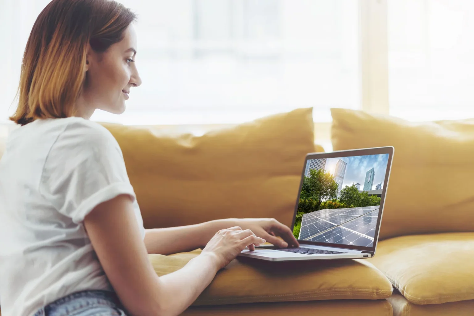 Eine junge Frau sitzt auf dem Boden ihres Wohnzimmers, den Ellbogen auf das Sofa gestützt, und informiert sich an ihrem Laptop über eine inflationssichere Geldanlage in Alternative Investmentfonds (AIFs).