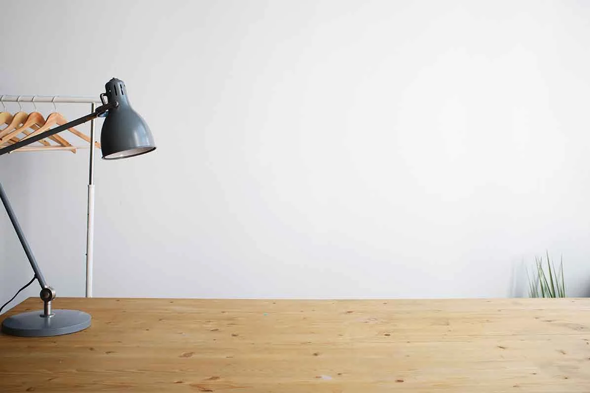 Ein leerer Schreibtisch mit einer Schreibtischlampe vor einer kahlen weißen Wand als Symbol für die Auswirkungen der Kurzarbeit auf Zahnärzte.