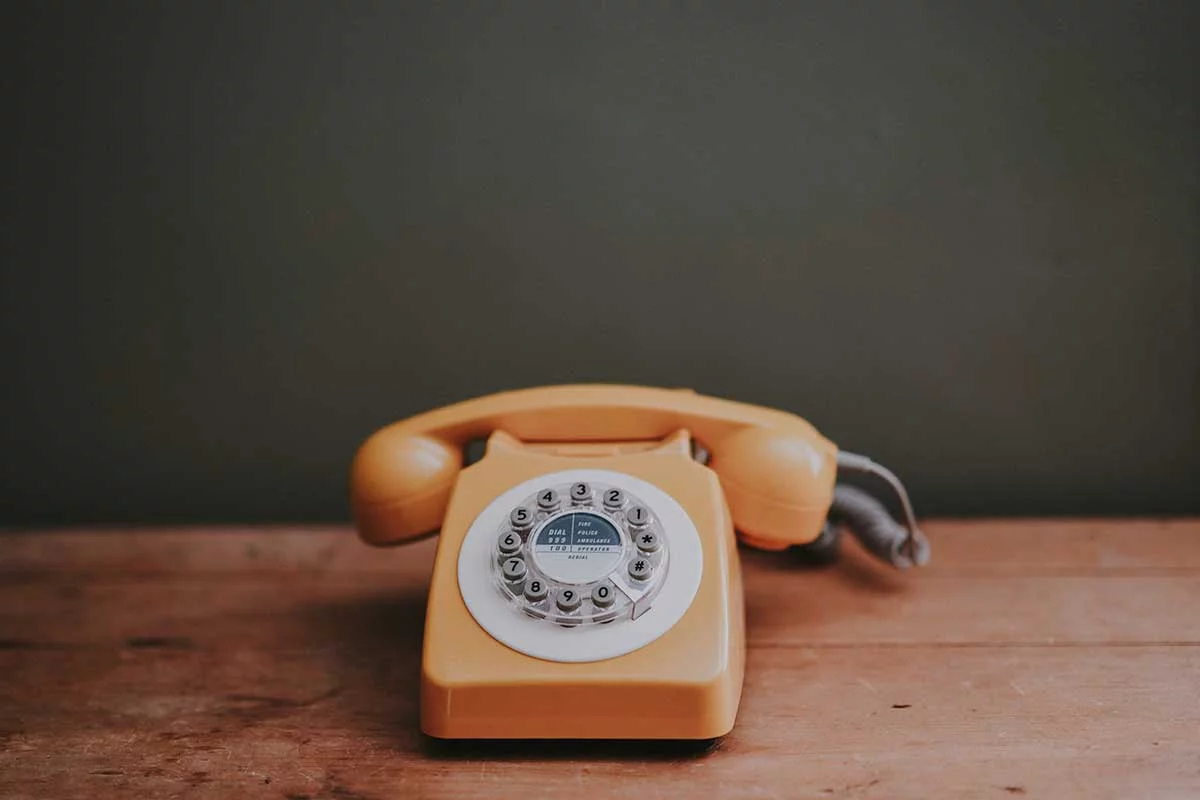 Ein orangefarbenes Telefon mit Wählscheibe auf einem Holztisch visualisiert, wie wichtig Nachsorgeanrufe für die Patientenbindung von Zahnärzten sind.