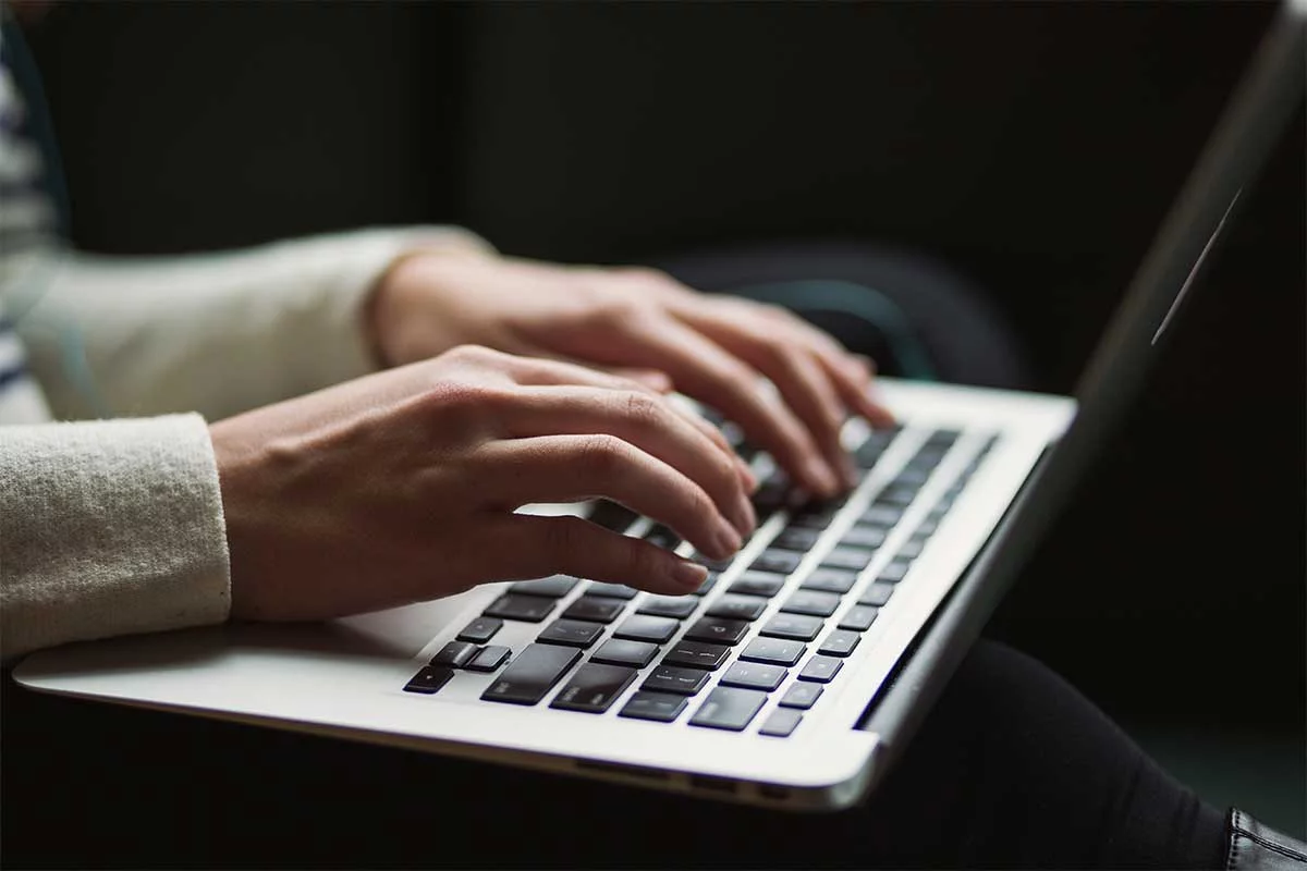 Nahaufnahme der Hände einer Patientin, die auf der Tastatur ihres Laptops eine Online-Bewertung für ihren Zahnarzt schreibt.