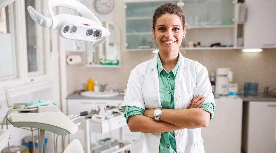 Eine junge Zahnärztin steht lächelnd im Behandlungszimmer – Symbolbild für das dental-start-Seminar zur Praxisgründung.